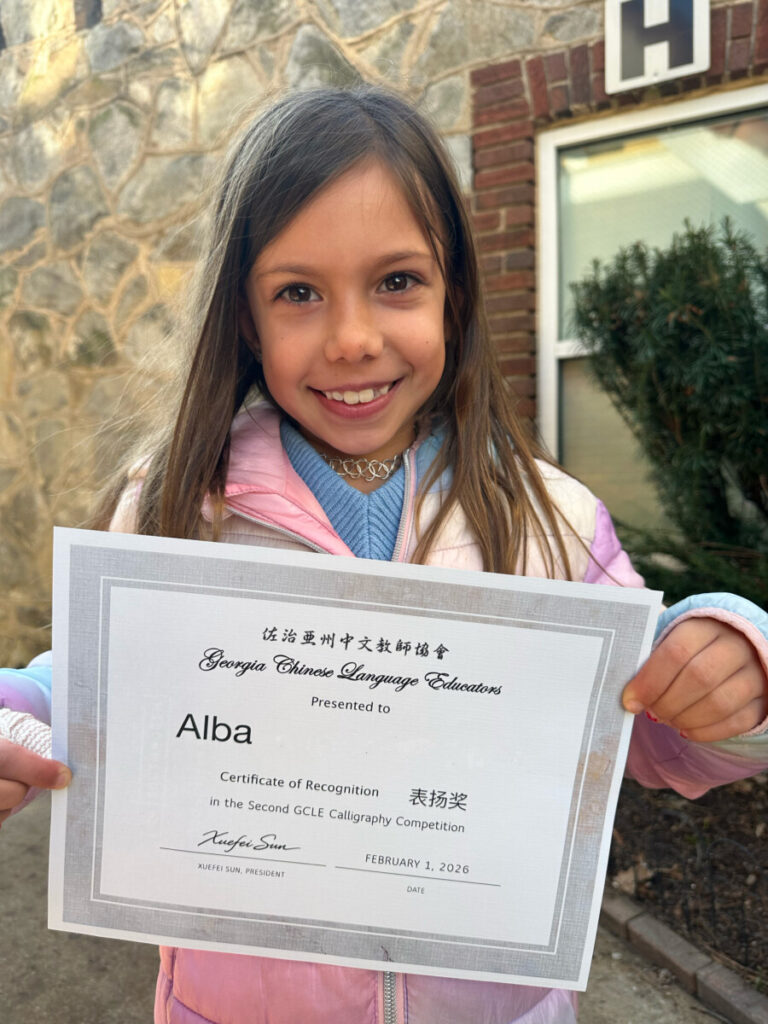 Second grade TCS student smiles and holds her certificate after being recognized in the Georgia Chinese Language Educators Hard Pen Calligraphy Competition.