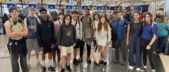 Cost_Rica_2026_Airport A large group of TCS middle school students and two adult chaperones pose together in the Delta terminal at Hartsfield-Jackson Atlanta International Airport, backpacks on and smiles ready, as they prepare to depart for their Costa Rica trip. The bustling airport terminal with Delta check-in kiosks and signage is visible in the background.